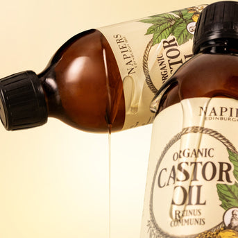 Two Napiers Organic Castor Oil bottles with oil streaming from tilted bottle