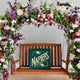 Floral archway with pink and purple flowers framing wooden bench displaying Napiers Stockists sign
