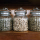 Glass storage jars filled with dried Goat's Rue herb leaves on wooden shelf