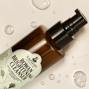 Napiers Rowan Brightening Cleanser spray bottle angled with water droplets on cream background